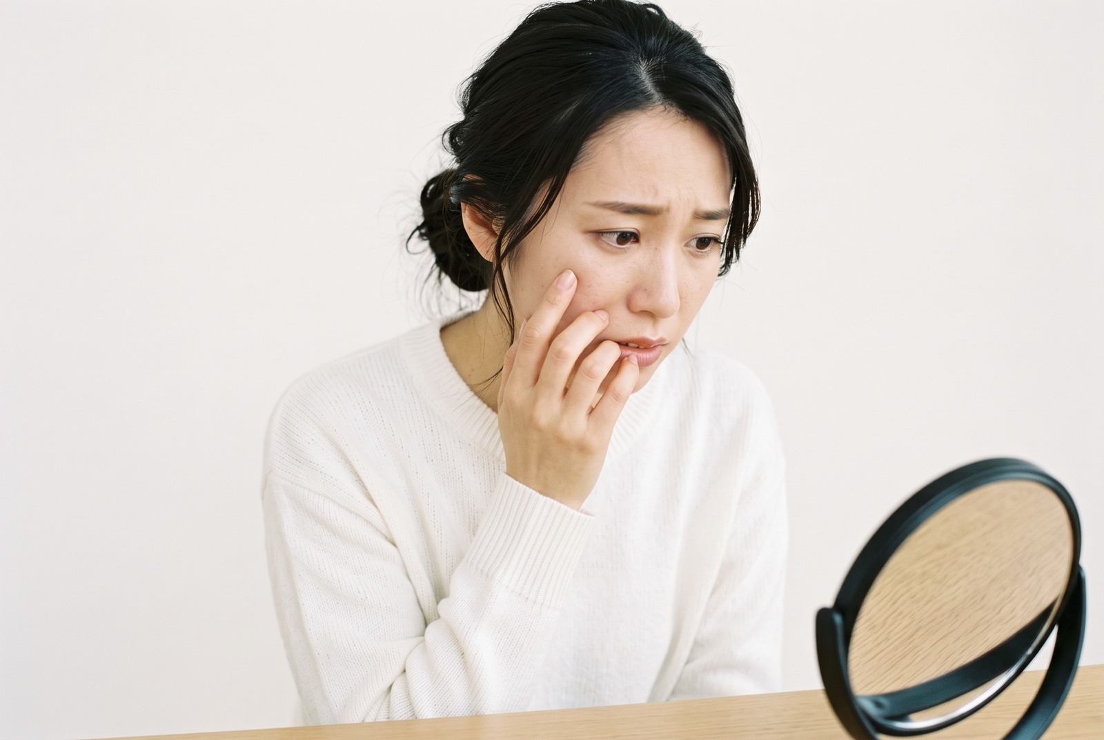 鏡を見ながら目の下を指で気にする女性