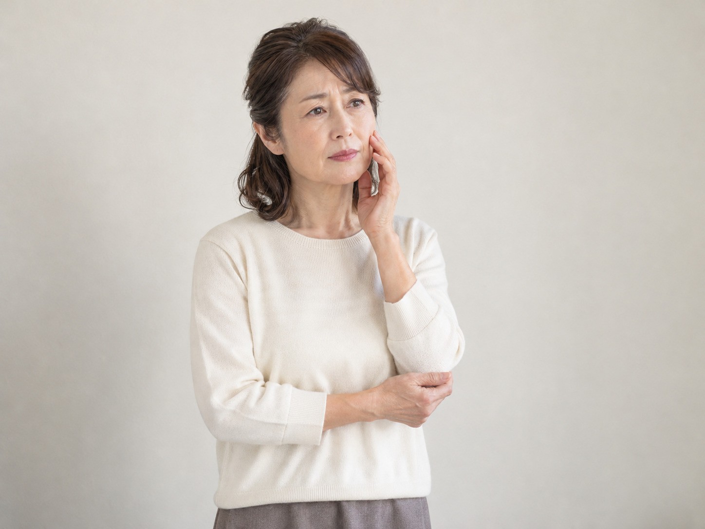立ったまま頬に手を当て、肌の乾燥やハリ不足を気にする女性